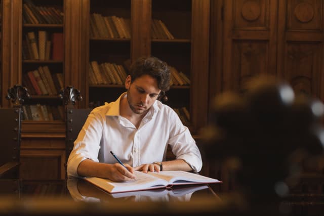 Davide Massiglia sitting in the room holding a red notebook and looking in the distance