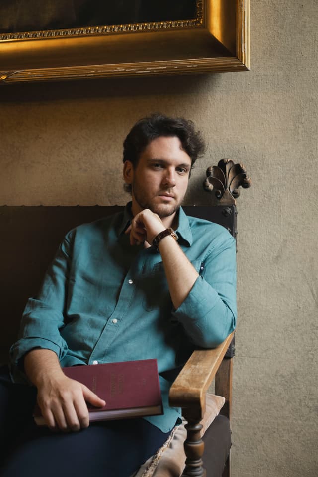 Davide Massiglia sitting in the room holding a red notebook